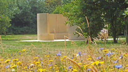 Photograph of the memorial with trees in the background and yellow and blue flowers in the foreground