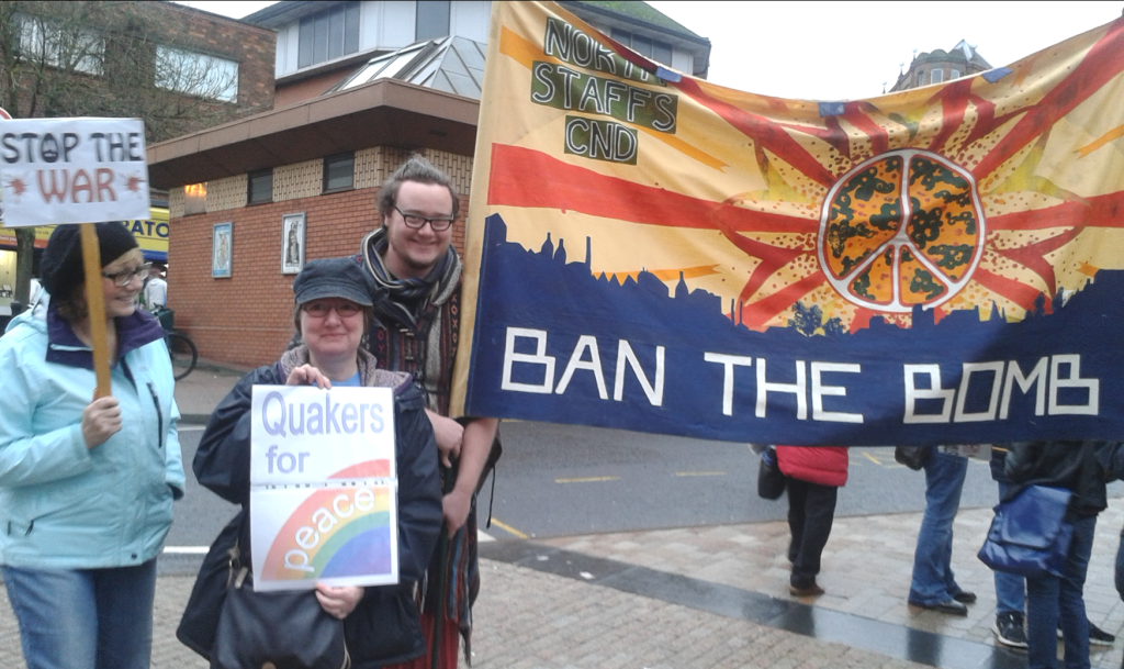 People at a protest with banners reading "Stop the War", Quakers for Peace" and "Ban the Bomb"
