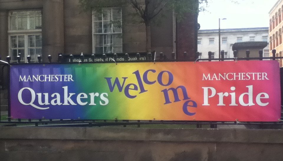Photo shows a rainbow banner attached to the railings outside Manchester Meeting House. It bears the words Manchester Quakers welcome Manchester Pride.